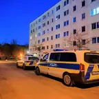 Zwei Polizeifahrzeuge stehen vor einem mehrstöckigen Wohnhaus in der Dämmerung, der Bereich ist mit Absperrband gesichert.