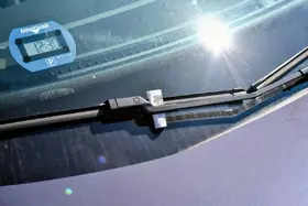Windschutzscheibe eines Fahrzeugs mit Parkscheibe und Knöllchen unter dem Scheibenwischer.