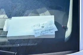 Zettel mit handschriftlicher Notiz liegt unter der Windschutzscheibe eines Fahrzeugs.
