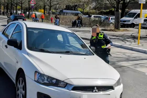 Polizistin mit Warnweste verteilt Knöllchen an weißen Mitsubishi-Pkw, der auf Radweg im eingeschränkten Halteverbot steht