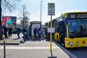 Menschen beim Ein- und Ausstieg an einer Bushaltestelle an einem gelb-schwarzen Bus der Linie X69.