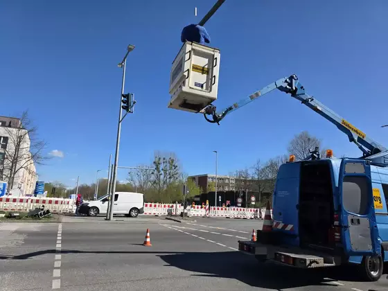 Blauer Transporter mit Steiger hebt einen Arbeiter in einem Korb an einer Ampelkreuzung