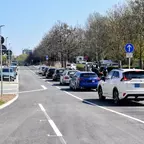 Straße mit wartenden Autos rechts und Fußgängern links bei sonnigem Wetter