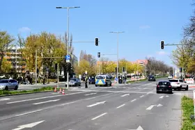 Breite Kreuzung mit mehreren Fahrspuren, an der eine Polizeistreife und mehrere Personen stehen, während die Ampeln ausgeschaltet sind.