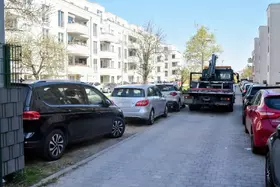 Enge Wohnstraße mit mehreren parkenden Autos auf beiden Seiten und einem Abschleppwagen, der offenbar ein falsch geparktes Fahrzeug abholt.