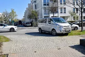 Silberner Transporter steht auf einer Einfahrt in einer städtischen Wohngegend mit mehrstöckigen Gebäuden.