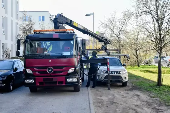 Rotes Abschleppfahrzeug mit ausgefahrenem Kranarm neben einem geparkten SUV auf einem Gehweg in Wohngebiet.