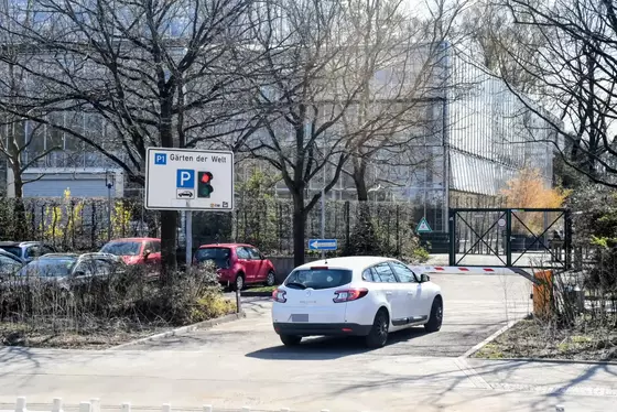 Weißer Renault steht vor roter Ampel und geschlossener Schrank, umgeben von Bäumen und weiteren geparkten Autos.