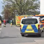 Polizeifahrzeug und Rettungswagen stehen auf einer Straße vor einem Sportplatz, mehrere Einsatzkräfte in Warnkleidung sind zu sehen