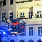 Feuerwehrmann auf einer Drehleiter vor einem mehrstöckigen Wohnhaus bei Nacht mit Blaulicht am Einsatzfahrzeug