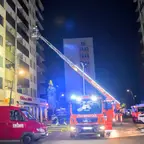 Feuerwehr mit ausgefahrener Drehleiter kontrolliert einen Balkon, nach einem Brand, eines mehrstöckigen Wohnhauses bei Nacht.