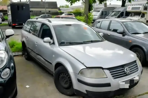 Beschädigter silberner VW-Kombi mit eingedrückter Fahrertür und abgefahrenem linken Vorderreifen auf einem Parkplatz zwischen anderen Fahrzeugen