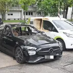 Ausgebrannter schwarzer Mercedes mit zerstörtem Dach und Innenraum steht auf einem Parkplatz neben einem weißen Transporter mit Brandspuren an der Seite.