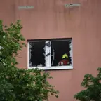 Fassade eines Gebäudes mit zerborstenem Fenster nach Explosion und Feuerwehrmann im Fensterrahmen