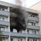 Mehrstöckiges Wohngebäude mit starkem schwarzen Rauch, der aus einem Balkon im mittleren Stockwerk aufsteigt.
