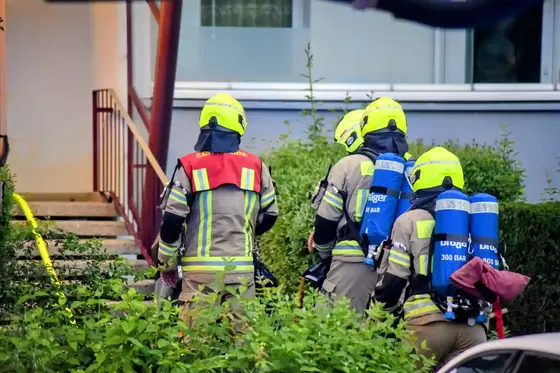 Vier Feuerwehrleute mit gelben Helmen und Atemschutzgeräten gehen auf ein Gebäude zu
