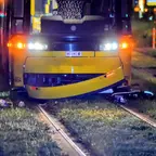 Straßenbahn steht nachts auf Gleisen mit unter dem vorderen Bereich eingeklemmtem Fahrrad und verstreuten Gegenständen