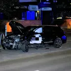 Schwarzer Toyota mit massiv beschädigter Front und geöffneter Motorhaube und Fahrertür steht nachts auf der Straße vor einem Biergarten