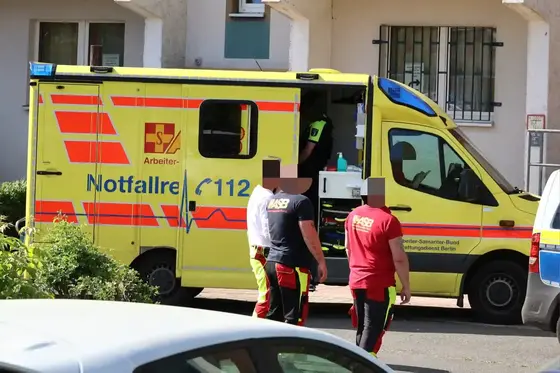 Gelber Rettungswagen mit geöffnetem Seitentür und drei Personen in Einsatzkleidung davor in einer Wohnstraße.