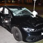 Schwarzer VW-Mietwagen mit eingedrückter Fahrertür, zertrümmertem Front- und Seitenscheiben sowie ausgelösten Airbags steht nach Unfall auf Straßenrand.