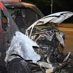 Ausgebrannter Transporter mit geöffnetem Motorraum und stark beschädigter Frontpartie auf einer Straße bei Nacht.