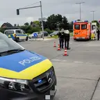 Polizeiwagen mit eingeschaltetem Blaulicht an einer Kreuzung, im Hintergrund Rettungswagen und Einsatzkräfte auf der Straße.