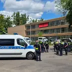 Mehrere Polizisten stehen vor einem mehrstöckigen Gebäude mit roten Markisen neben einem weißen Polizeifahrzeug