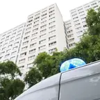 Blick von unten auf ein Hochhaus mit mehreren Fenstern und einen Teil eines Einsatzfahrzeugs mit blauem Blaulicht im Vordergrund.