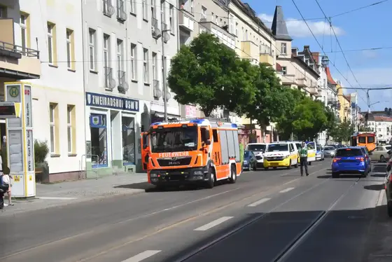 Straße mit mehrstöckigen Wohnhäusern, einem Feuerwehrfahrzeug, mehreren Einsatzfahrzeugen der BVG und einer Person in Uniform auf der Straße.