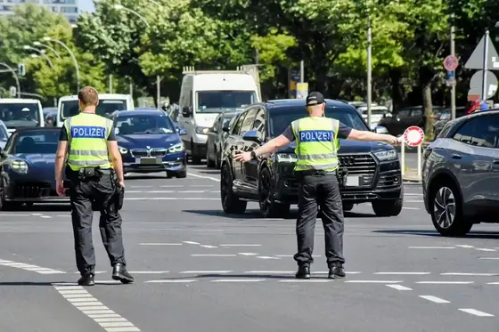 Zwei Polizisten sperren eine Straße, einer hält eine Polizeikelle in der Hand, mehrere Fahrzeuge warten im Hintergrund