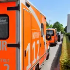 Mehrere Einsatzfahrzeuge der Berliner Feuerwehr stehen an einer Straße neben einem Wohnhaus und einer Hecke