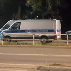 Zwei weiße Einsatzfahrzeuge mit blauen Streifen und den Aufschriften "GERICHTSMEDIZIN" und "POLIZEI" stehen nachts an einer Straße hinter einem Geländer.