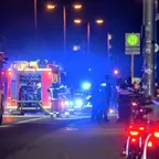Feuerwehrautos mit eingeschalteten Blaulichtern und Einsatzkräften auf einer Straße bei Nacht neben einer Bushaltestelle.