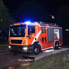 Feuerwehrfahrzeug mit eingeschaltetem Blaulicht steht nachts auf einer Straße.