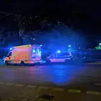 Rettungswagen und Polizeiauto mit eingeschaltetem Blaulicht stehen nachts vor einem Gebäude.