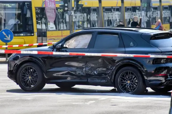 Schwarzes SUV mit großer Delle an der Fahrertür steht vor einer gelben Straßenbahn und ist von Absperrband umgeben.