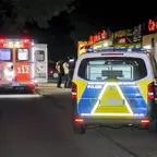 Einsatzfahrzeuge von Feuerwehr und Polizei stehen nachts vor einem Dönerladen, drei Personen unterhalten sich auf der Straße.