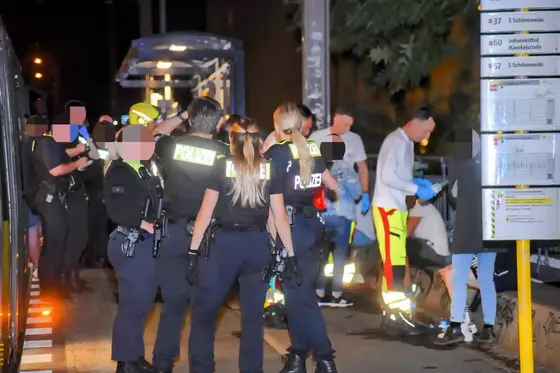 Mehrere Polizisten und Rettungskräfte mit Augenspülflasche versorgen mehrere Patienten an einer Straßenbahnhaltestelle bei Nacht.