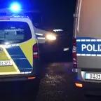 Drei Polizeifahrzeuge mit Blaulicht in der Nacht, eines mit gelb-blauem Muster und die anderen beiden mit blauem Streifen