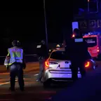 Polizisten in Warnwesten stehen nachts auf der Autobahn neben einem weißen Auto mit eingeschaltetem Rücklicht, im Hintergrund Blaulicht und Feuerwehrfahrzeug