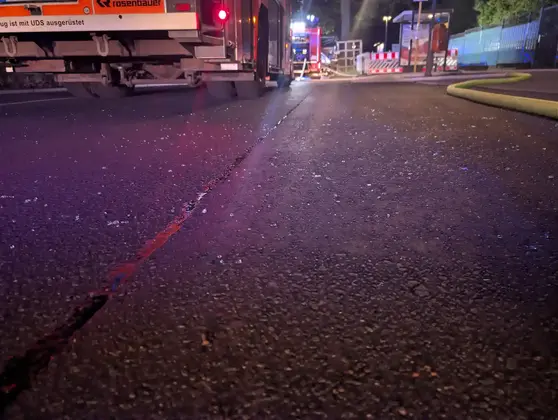 Glasplitter liegen auf einer Straße vor Feuerwehrfahrzeugen mit eingeschaltetem Warnlicht.