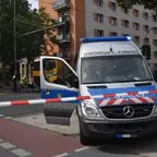 Polizeiwagen mit geöffneter Tür und eingeschaltetem Blaulicht steht an einer abgesperrten Kreuzung, im Hintergrund Einsatzkräfte und ein Fahrrad neben einem LKW sichtbar