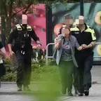 Polizisten führen eine Frau nach einer Geiselnahme in einem Supermarkt, umgeben von Einsatzkräften und einem Notarzt in gelber Schutzkleidung.