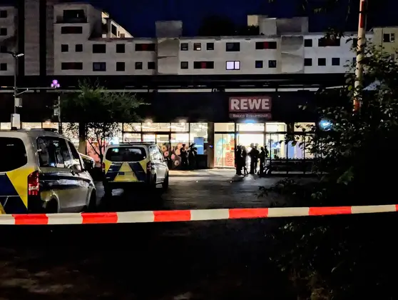 Polizei und SEK stehen nachts vor dem Eingang eines REWE-Supermarkts, abgesperrt mit rot-weißem Flatterband.