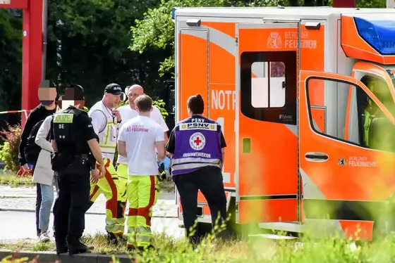 Mehrere Einsatzkräfte, darunter Polizisten und Rettungssanitäter, stehen neben einem geöffneten Rettungswagen der Berliner Feuerwehr