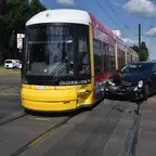 Straßenbahn und schwarzes Auto mit beschädigter Front stoßen auf Straßenbahngleisen zusammen.