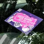 Auf der Windschutzscheibe eines Autos liegt ein lila Aufkleber mit der Aufschrift 'DIESE KARRE IST ZU FETT!' und einer stilisierten Zeichnung eines Autos.