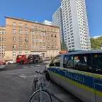 Polizeiwagen und Feuerwehrfahrzeuge vor einem mehrstöckigen Wohngebäude an einer Straßenecke bei klarem Himmel