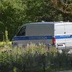Weiß-blauer Transporter mit der Aufschrift 'GERICHTSMEDIZIN' steht auf einem Weg vor grünem Bewuchs