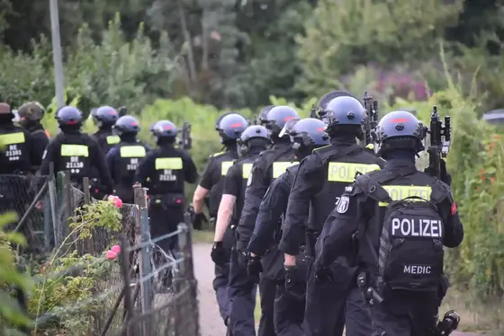 Gruppe von Polizisten in Schutzkleidung und Helmen geht auf einem schmalen Weg durch einen Gartenbereich
